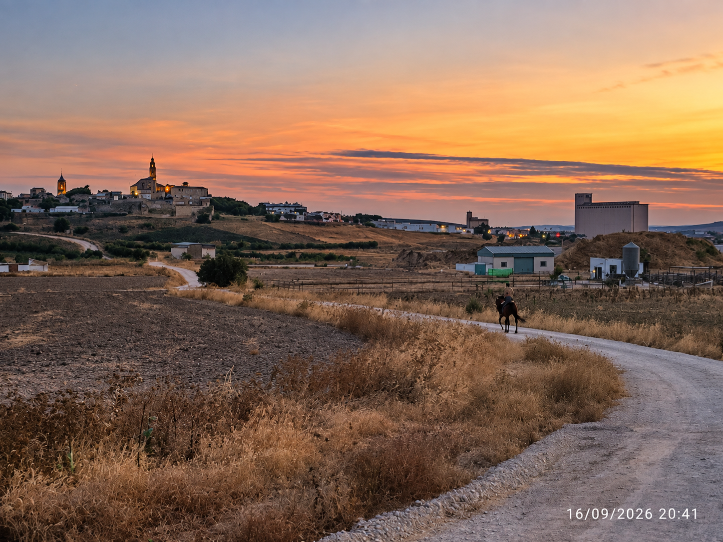 Camino rural de Marchena al atardecer con un jinete y el pueblo al fondo