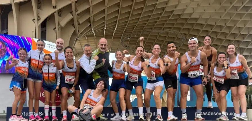 Grupo de corredores del Marathón Marchena en Sevilla junto al cartel de la carrera Casco Antiguo